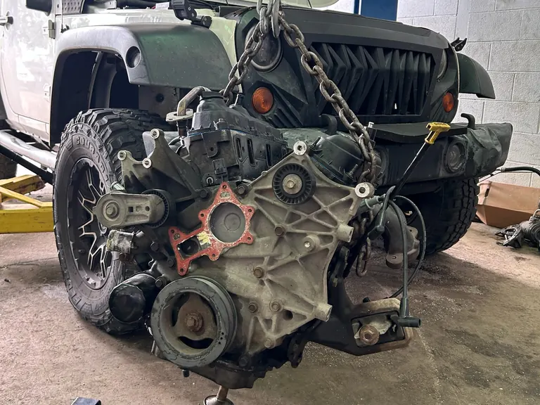 Engine being lifted out of a Jeep with a hoist chain in a Motorpool service bay